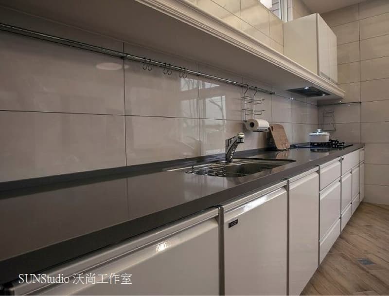 這張照片是一個現代化的廚房，最重要的部分是流理台，它由深色石材製成，上面有一個銀色的水槽和一個銀色的水龍頭。流理台的下方是白色櫥櫃，非常簡潔明亮。