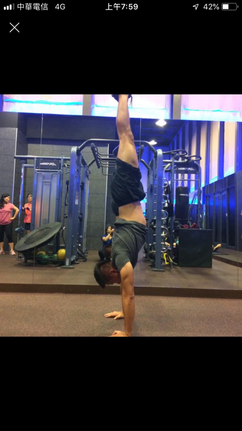 這張照片是一名男子在健身房做倒立的動作，他的雙手撐著地面，雙腳朝天，看起來很輕鬆，也顯得很有力量。