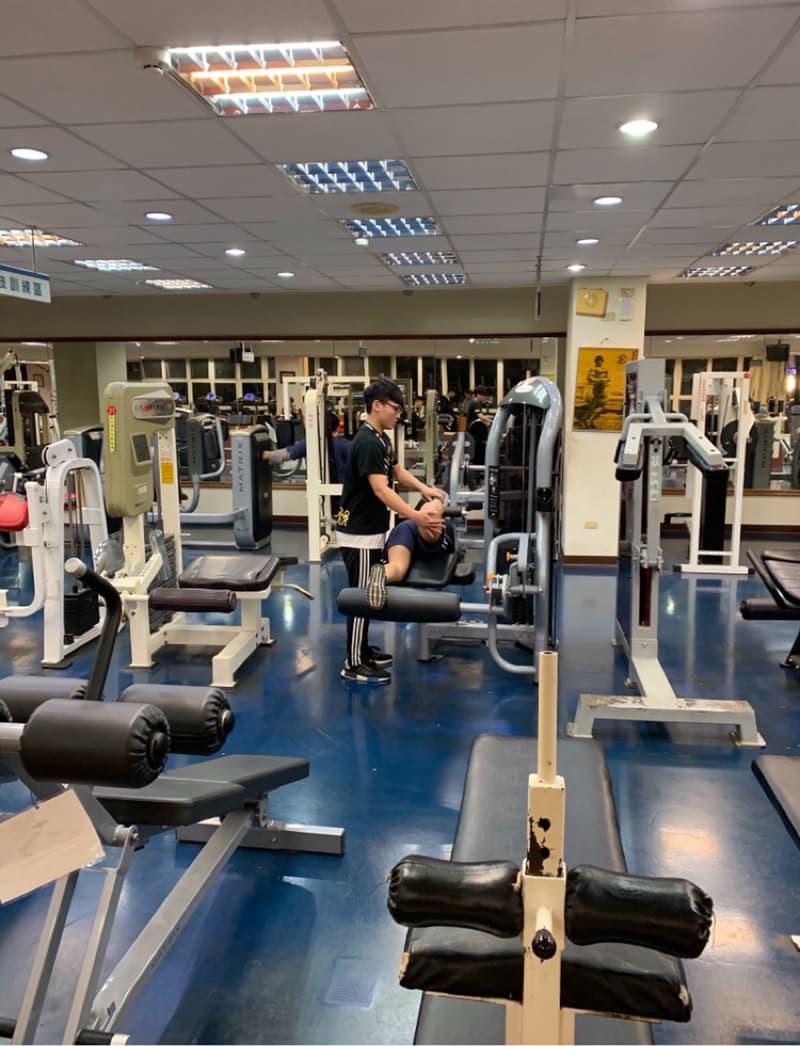 這張照片是一個健身房，照片的中心位置有一個正在使用器械的男性。