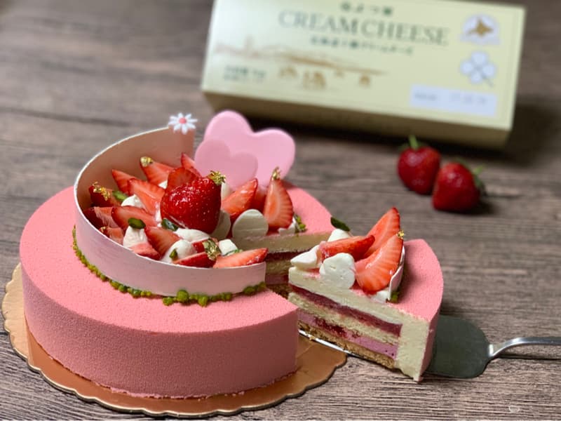 這張照片是一塊草莓慕斯蛋糕。蛋糕的形狀是圓形，外層覆蓋著粉紅色的慕斯，中間夾著一層白巧克力慕斯，最底部是草莓果醬。蛋糕上擺滿了新鮮的草莓，看起來非常誘人。