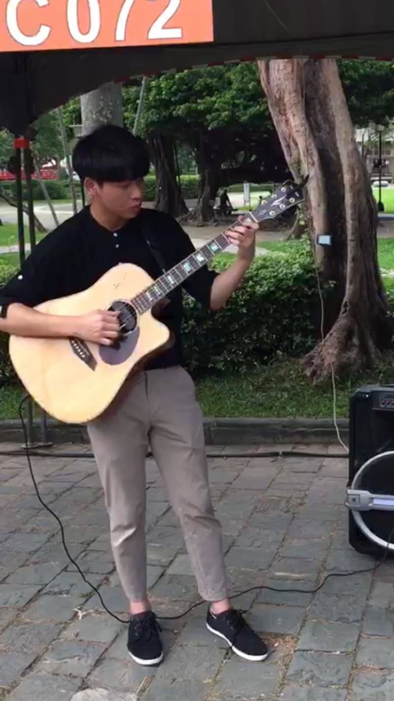 這張照片是一個年輕人在戶外彈吉他，他正在用吉他演奏音樂，畫面中也有一個擴音器，可能是他正在街頭表演。