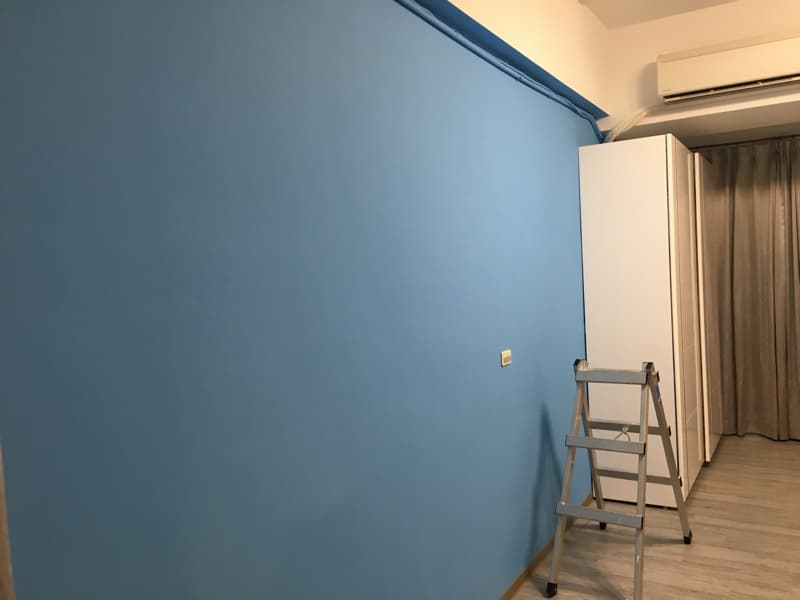 這張照片是一面藍色的牆壁，牆壁上有白色的插座，牆壁前面放著一個銀色的梯子。