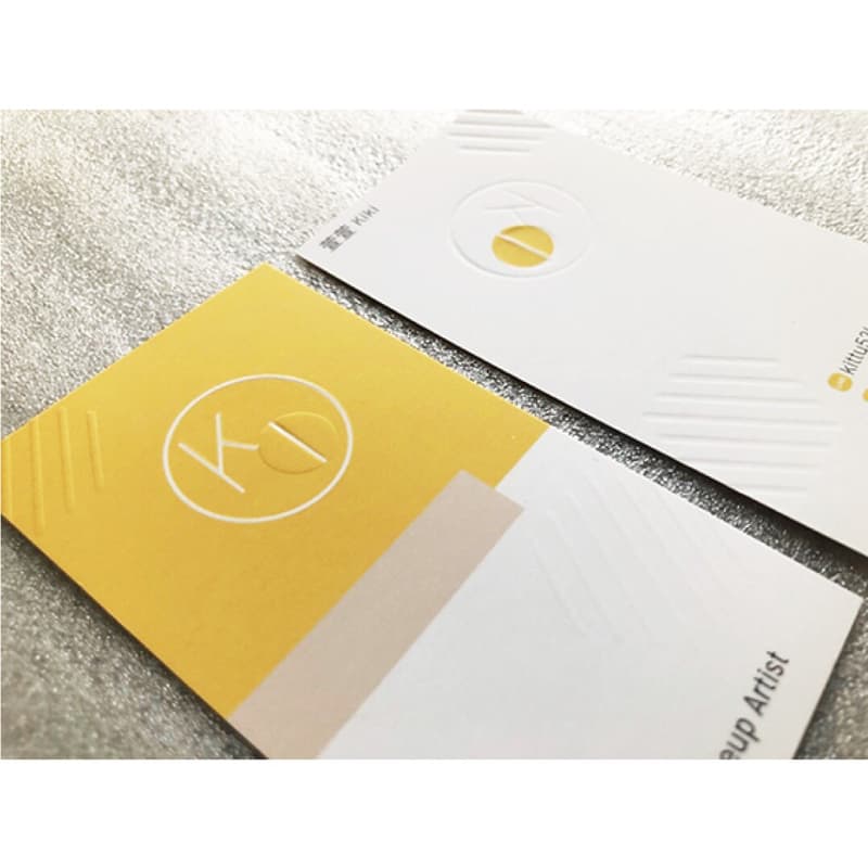 這張照片是兩張名片，其中一張是黃色的，上面有一個白色的圓圈，裡面寫著「K」；另一張是白色的，上面有幾條白色的線，以及一個小的圓圈，裡面是一個字母「K」。