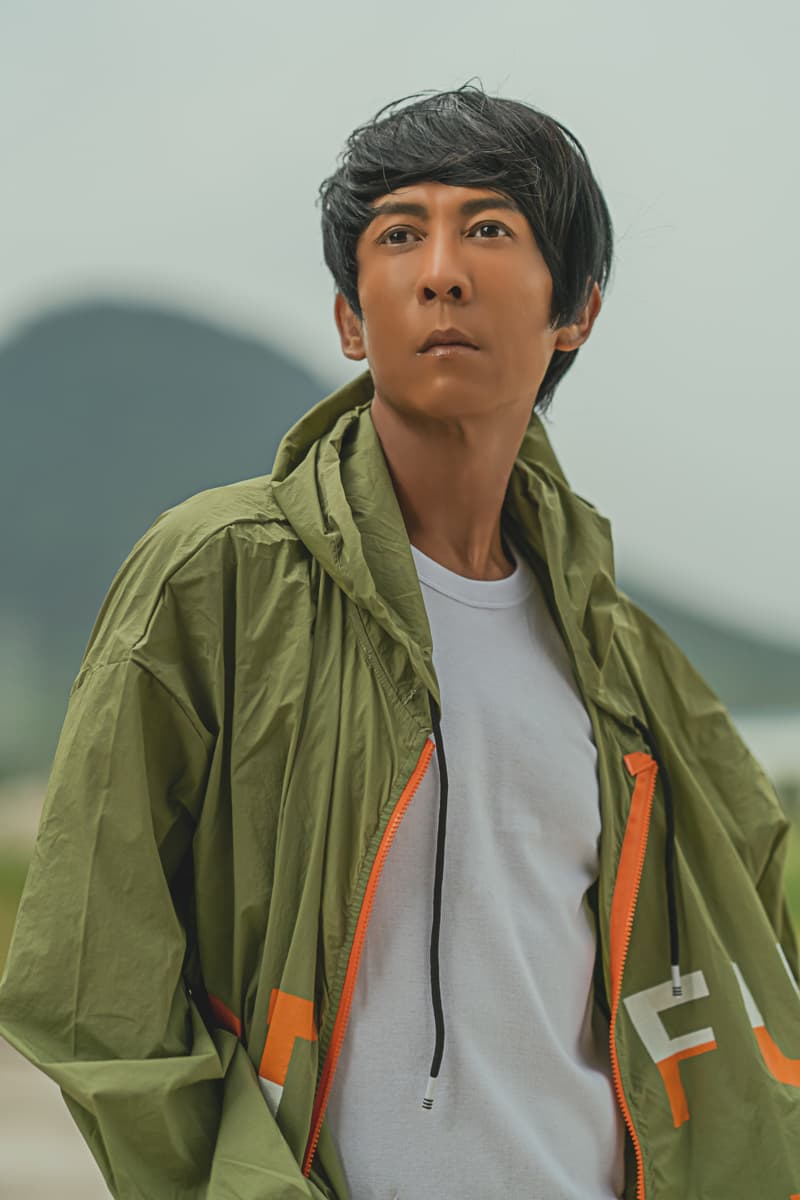 這張「年輕男子穿著綠色夾克站在戶外」的照片是，男子戴著帽子，望向遠方，看起來很冷靜。