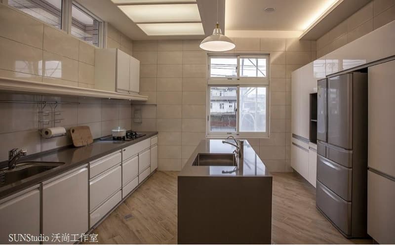 這張照片是一個現代化的廚房，最重要的部分是中央的白色大理石中島，上面擺放了一個水槽和兩個水龍頭，看起來非常乾淨整潔。