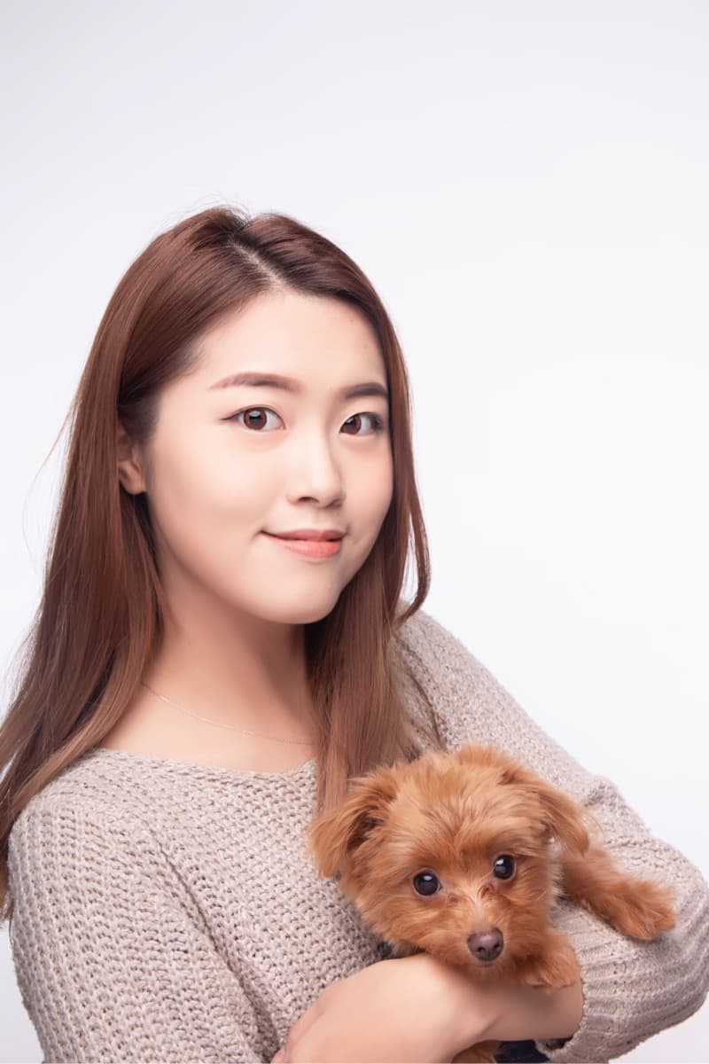 這張「一位年輕女子抱著一隻小狗」的照片是，女子穿著米色毛衣，她擁抱著一隻棕色的小狗，小狗看起來很可愛。