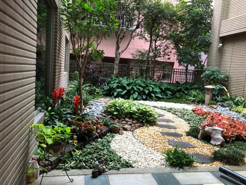 這張照片是一座帶有石頭小徑的花園，花園中點綴著許多綠色植物和紅色花朵，讓人感到舒適和放鬆。