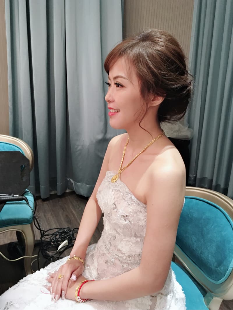 這張「新娘」的照片是穿著白色蕾絲婚紗，坐在藍色椅子上，並戴著金項鍊和金手鍊，看起來非常美麗動人。