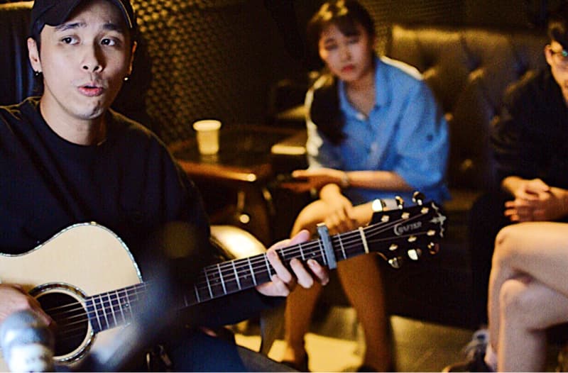 這張「音樂工作室」的照片是一個戴著帽子的男生正在彈吉他，旁邊坐著一個女生，而另一邊則坐著一個模糊的男生。