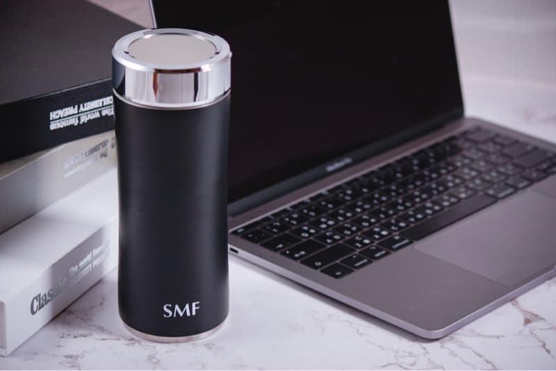 這張照片是一個黑色的水瓶，水瓶上有銀色的蓋子，蓋子上印有“SMF”字樣。水瓶放在一個白色大理石桌子上，桌子上還有一臺筆記型電腦。