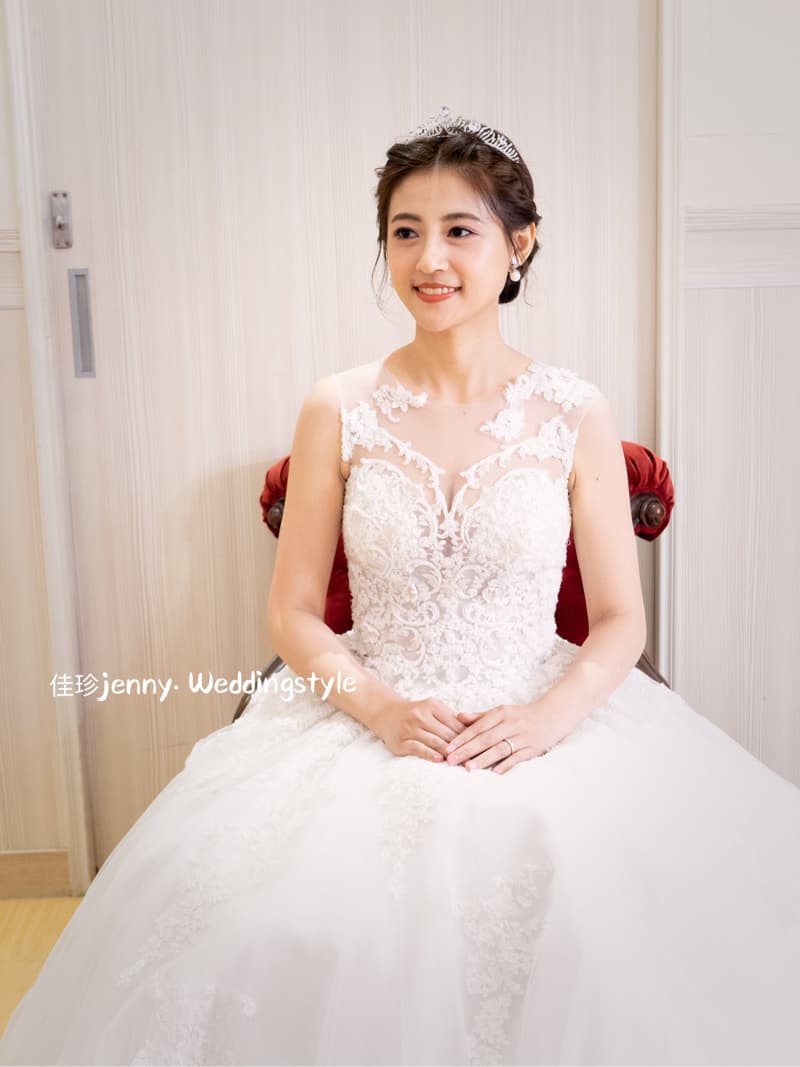 這張「婚紗照」的照片是一位穿著白色蕾絲婚紗的新娘，她戴著皇冠，坐在紅色椅子上，笑容甜美。