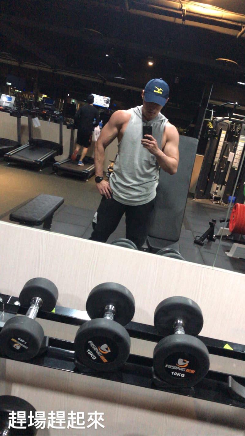這張「健身房」的照片是，一個戴著帽子，穿著運動服裝的男士，在健身房自拍，他身後有跑步機，背景是健身房的鏡子，鏡子反射出啞鈴架，架上放著兩組10公斤的啞鈴。