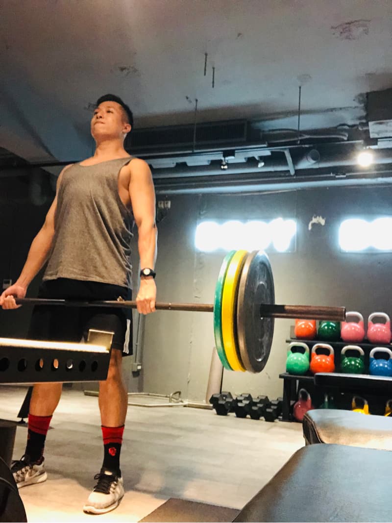 這張照片是一個男子在健身房舉重。他正在舉一個槓鈴，上面有幾個重量片。他看起來很努力，而且汗流浹背。