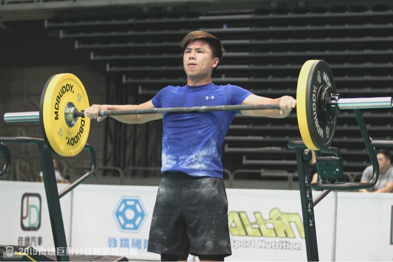 這張照片是一個年輕男子在舉重，他正在舉起一個槓鈴，臉上充滿專注的表情，顯示出他對運動的熱情和努力。