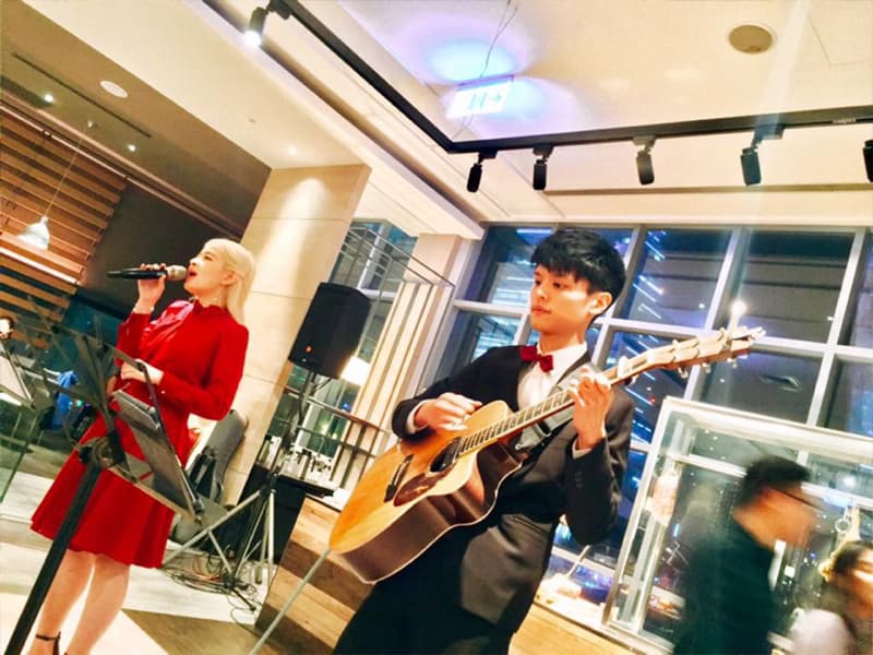 這張照片是一個男女二重唱在表演，女歌手穿著紅色的洋裝，正在唱歌，男歌手穿著西裝，彈著吉他。