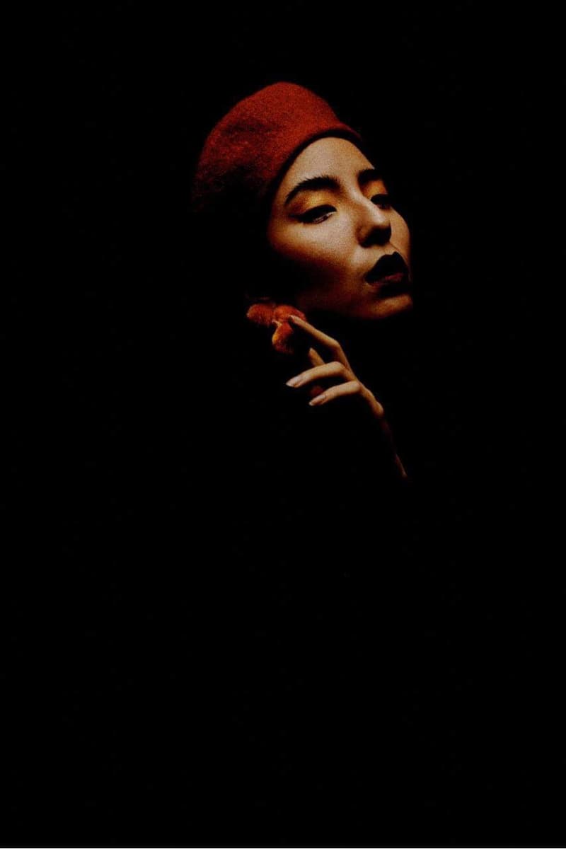 這張照片是一個戴著紅色貝雷帽的女性，她的臉被光線照亮，嘴唇塗著紅色的口紅，看起來很迷人。