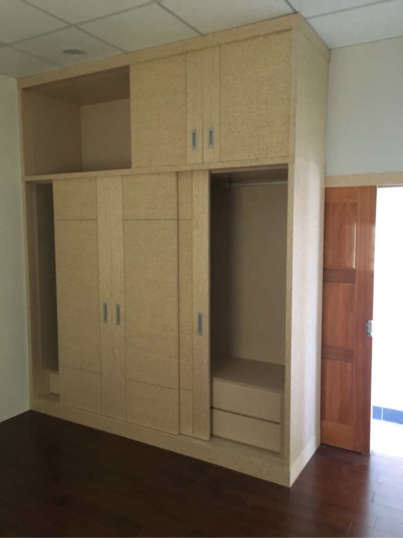 照片顯示一個木製衣櫃，衣櫃有兩個抽屜和一扇滑動門，衣櫃的右側有一扇木門，地板是木地板