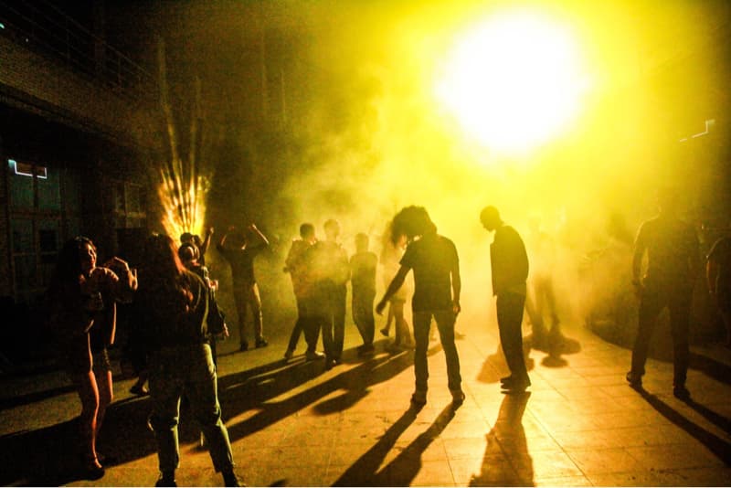 這張「一群人站在昏暗的場地中，他們被燈光照亮，並且在霧氣中跳舞」的照片是。