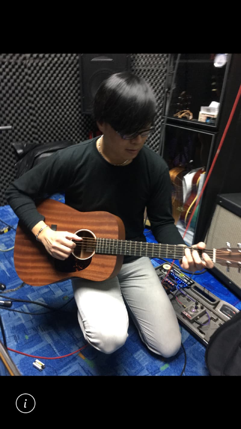 這張照片是一名男子坐在錄音室裡彈著一把木吉他。