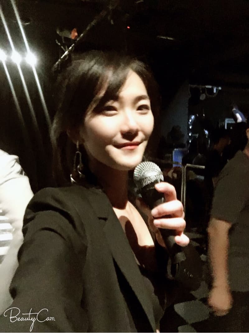 這張「一位年輕女子手持麥克風，身穿黑色西裝外套，背景是模糊的舞臺」的照片是。