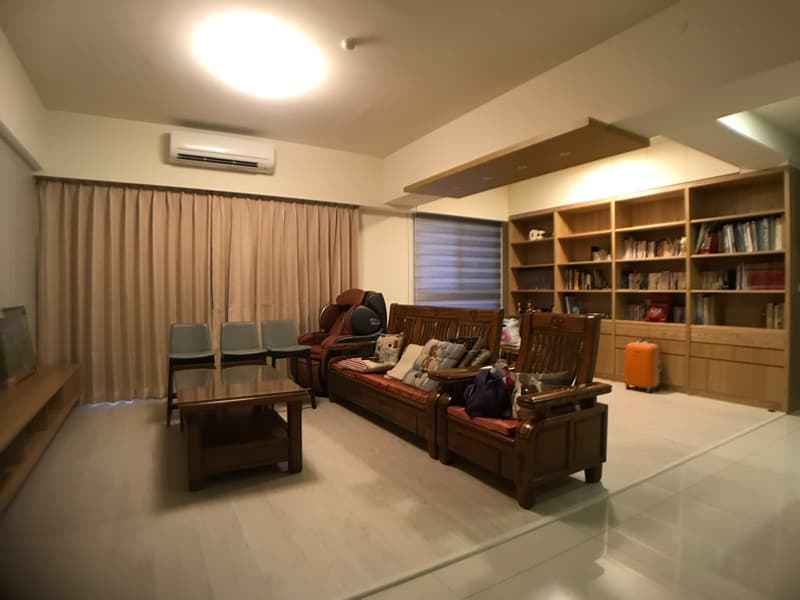 1) 照片顯示一個現代化的客廳，裡面的傢俱以淺色木頭為主， 沙發是淺棕色的布藝材質，房間的牆壁為白色，地板是淺色木地板