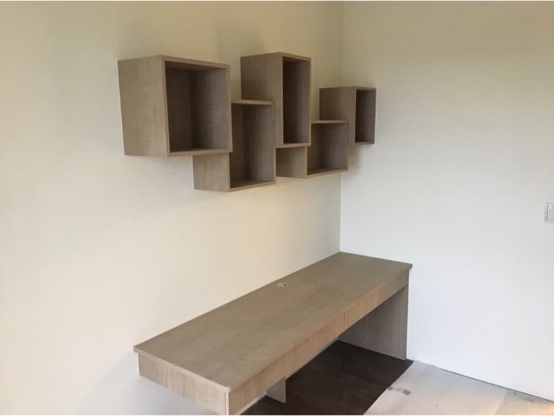 這張照片是一張書桌，書桌上的桌面是淺色的木板，桌面上有兩個抽屜，書桌的牆壁上有一個木質的隔板，隔板是多個小格子組成的。