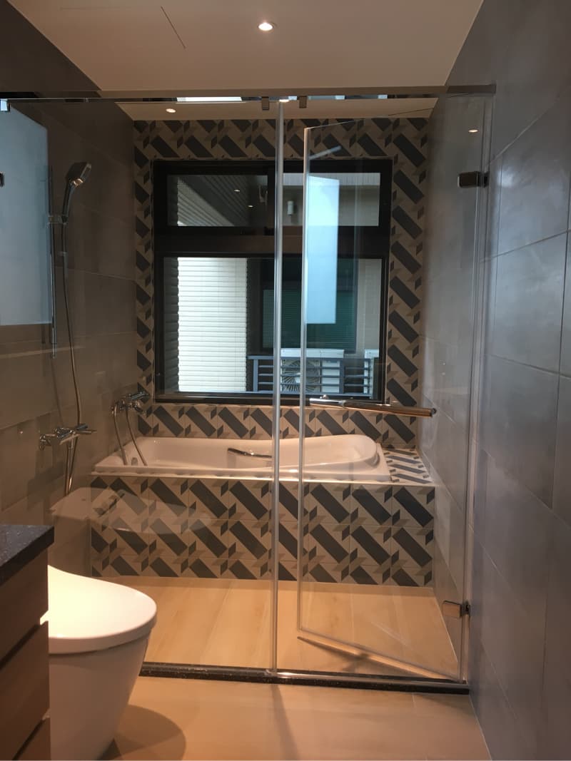 這張照片是一個現代化的浴室，裡面有一個浴缸和一個淋浴間，它們被玻璃隔開，牆壁上铺着几何形状的瓷砖，地板是浅色的木质地板。