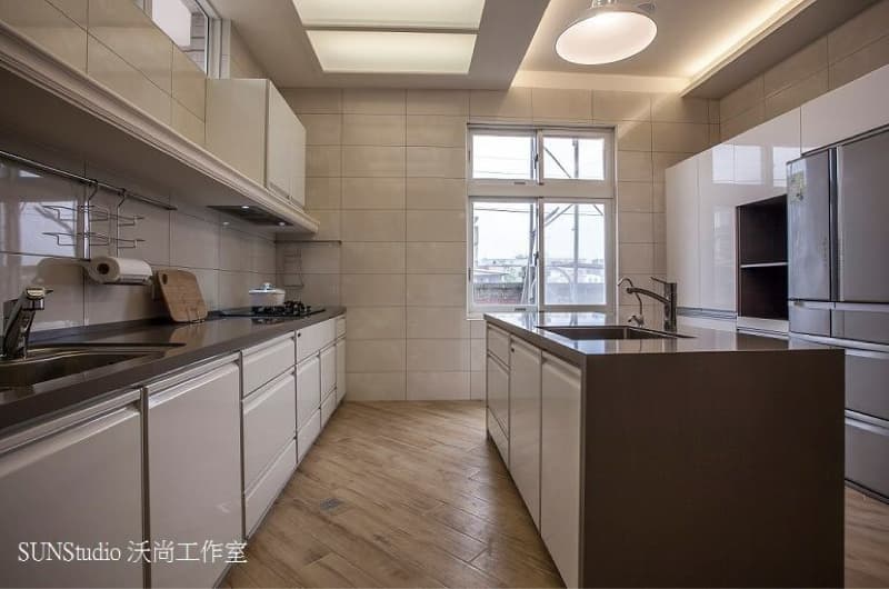 這張照片是現代化的廚房，廚房中島是照片中最顯眼的部分，中島上有個水槽，旁邊放著一組白色的櫥櫃，中島的檯面是深色的，與櫥櫃形成對比，看起來很時尚。