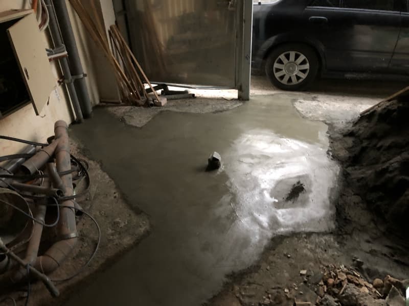 這張照片是正在施工的車庫，照片中最重要的部分是新鮮的水泥地面，水泥表面濕潤，還未完全乾燥，可以看到一些工具和材料散落在周圍。