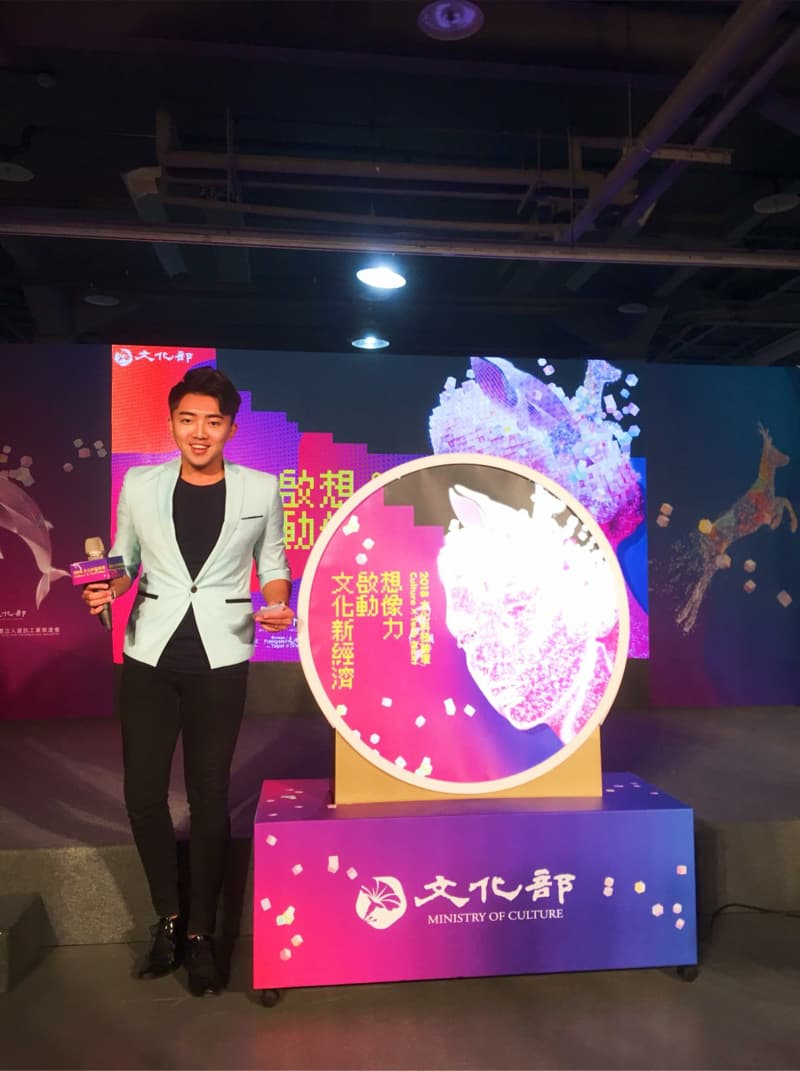 這張「文化部」的照片是一名穿著淺藍色西裝的年輕男性站在一個圓形裝置前，圓形裝置的背景是彩色的圖案，並且印有「文化部」的字樣。