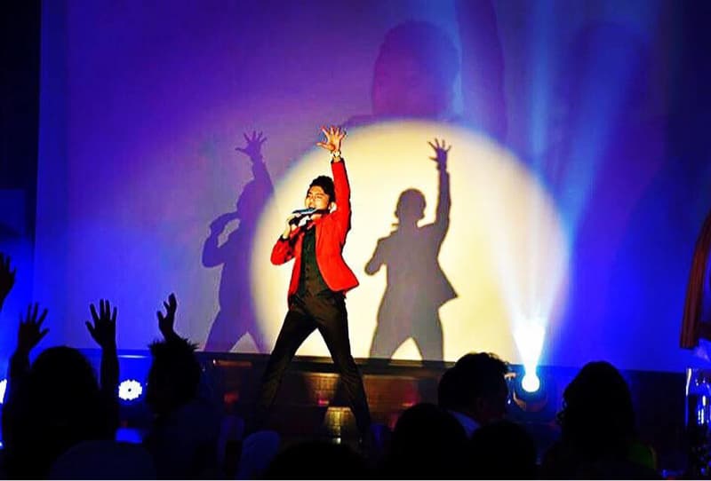 這張「演唱會」的照片是一個歌手在臺上唱歌，他穿著紅色外套，背景是藍色的燈光，臺下有很多觀眾。