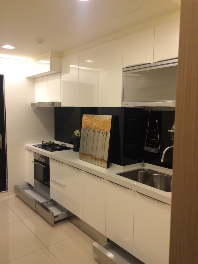 這張照片是一間現代化的廚房，最顯眼的是流理台下方的抽屜。抽屜設計成金屬色，與白色櫥櫃形成對比，讓空間更具層次感。