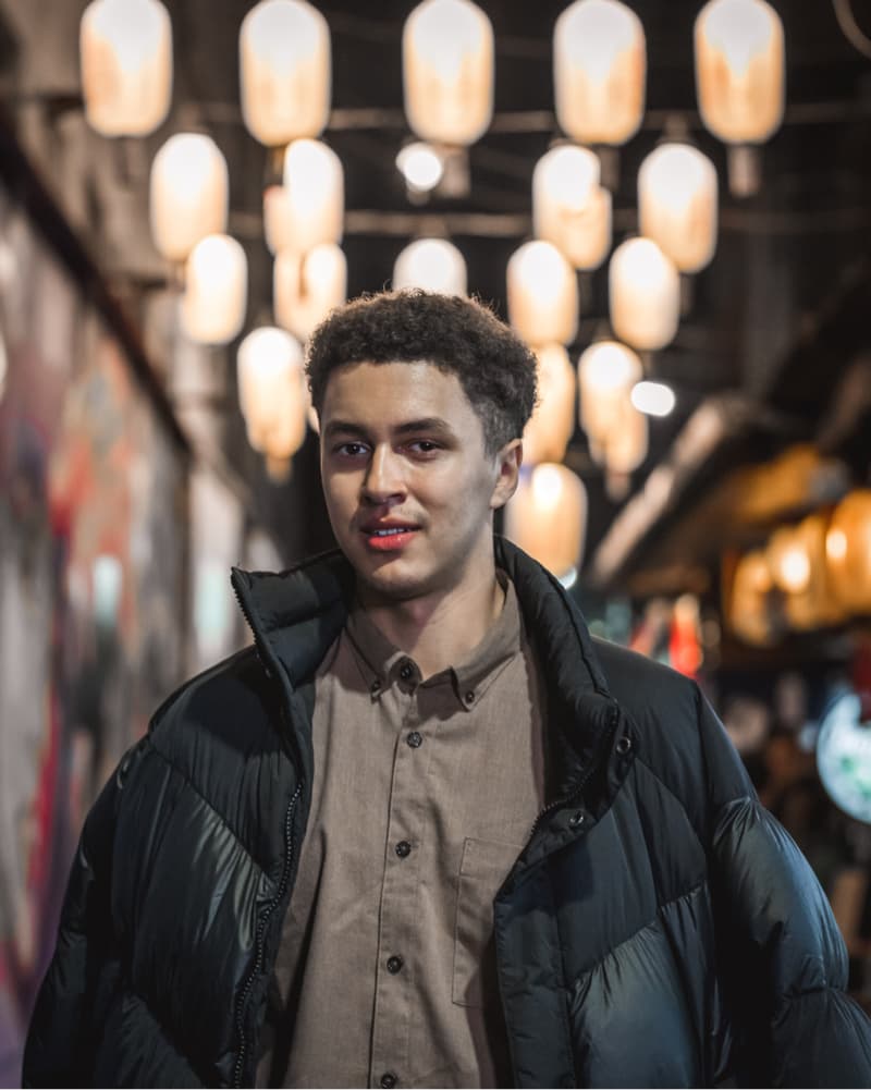 這張「年輕男子穿著深色外套，站在燈光昏暗的街頭」的照片是。