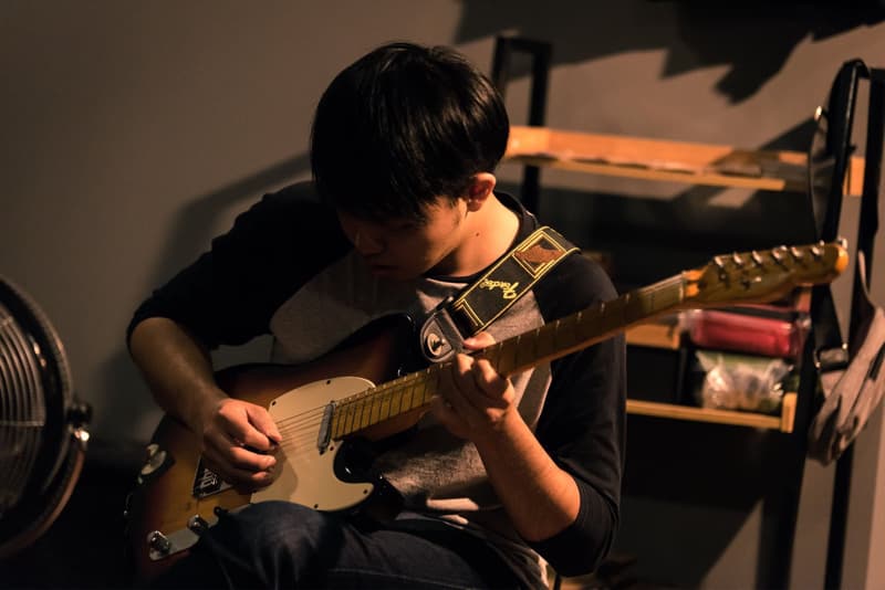 這張照片是一個年輕人彈著電吉他，他專注地看著琴弦，神情專注。