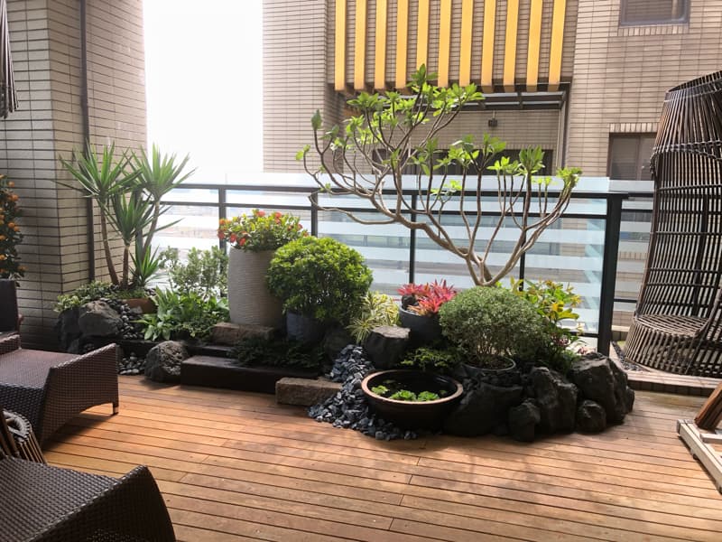 這張照片是一片陽臺，陽臺上擺放著許多盆栽植物，還有小型的假山造景，顯得十分幽靜舒適。