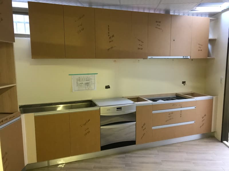 這張照片是一個廚房的裝修工程。照片中最重要的部分是新的流理台，包含水槽、烤箱、抽屜，並且已經裝設完成。流理台的櫃體是木頭材質，並有銀色的把手。