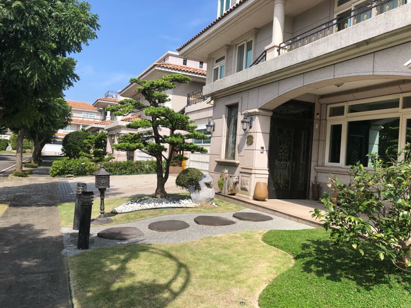 這張照片是一棟現代化的別墅，它的重點是別墅的入口，入口處有一個精緻的鐵門，兩旁有綠色植栽，前方有石頭鋪成的步道，別墅的外觀看起來很漂亮，整體設計風格典雅時尚。