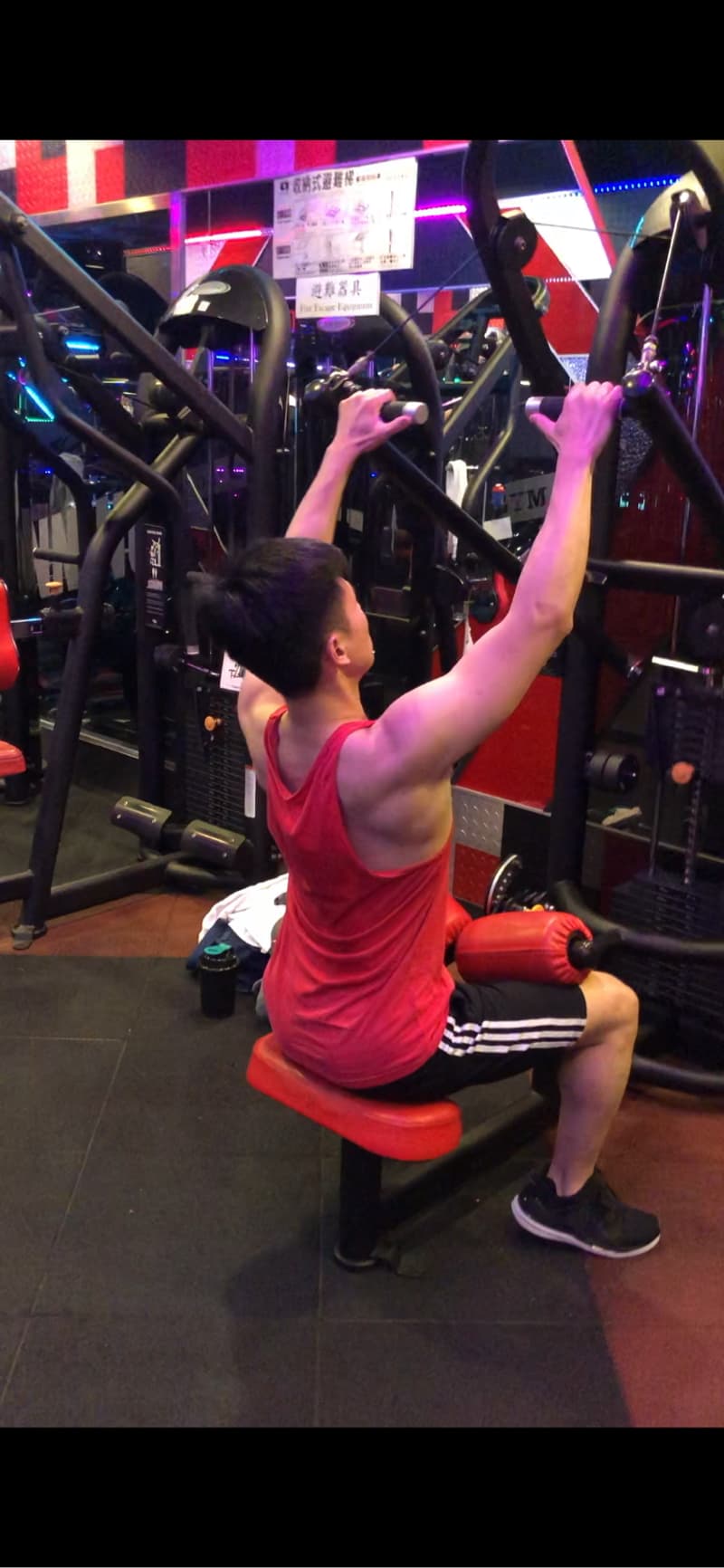 這張照片是一個年輕人在健身房裡用拉力器鍛鍊背部肌肉。他正用雙手握住拉力器的把手，向下拉動，看起來很努力。