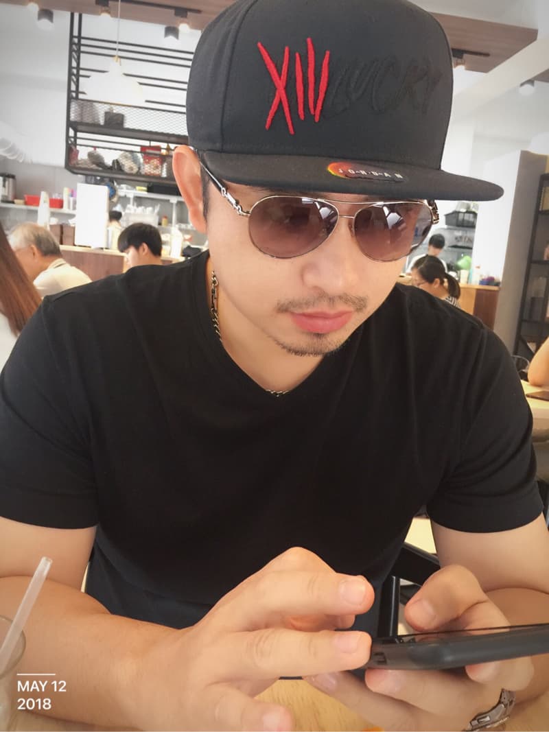 這張照片是一個男人在咖啡店裡低頭看手機。他戴著黑帽和墨鏡，穿著黑色的T恤，看起來很專注。