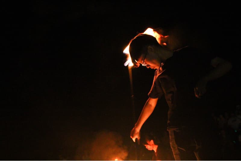 這張「火把表演」的照片是一名年輕男子在黑暗中表演火把，他戴著眼鏡，頭上纏繞著火焰，姿勢看起來很專業。