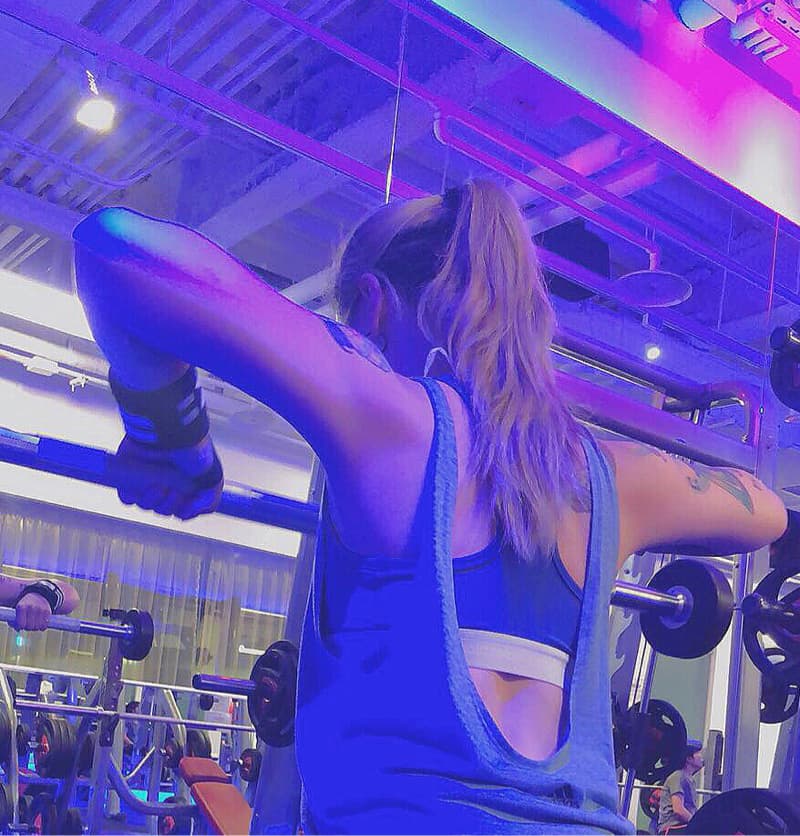 這張照片是一個女孩在健身房裡舉重，她戴著護腕，正努力地完成舉重動作，展現出她強健的肌肉和毅力。