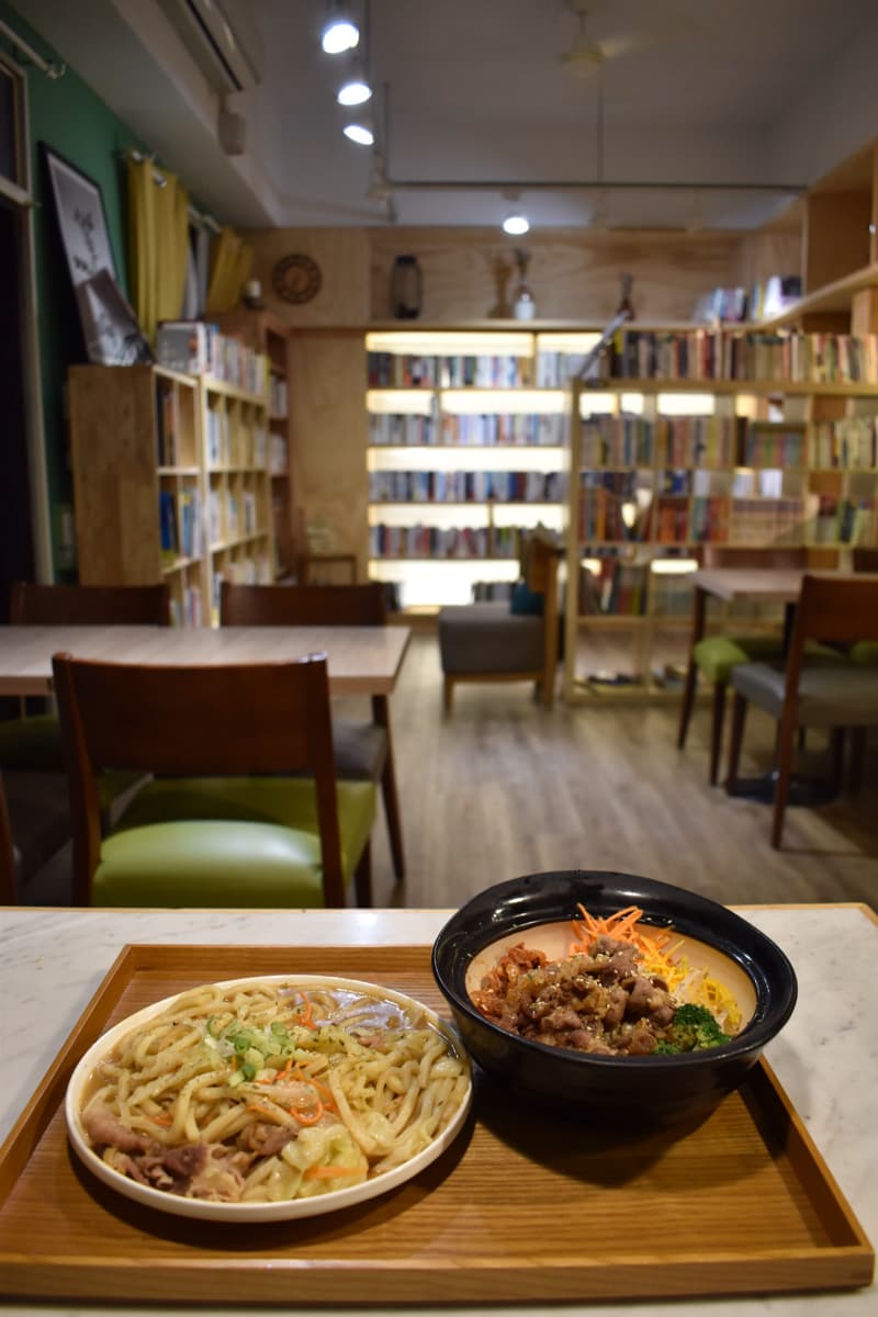 這張「餐廳」的照片是一個有書架的餐廳，桌上放著兩碗食物，一碗是烏龍麵，另一碗是肉燥飯。