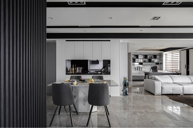 這張「現代風格住宅」的照片是，房間裡以黑白灰為主色調，帶有木質裝飾。中間是餐桌，旁邊有椅子，後面是廚房和餐櫃。右邊是客廳，擺放了白色沙發和書架。房間整體明亮整潔，展現了簡約時尚的風格。