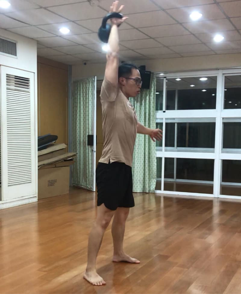 這張照片是一個男人正在進行舉重訓練，他右手舉起一個黑色壺鈴，身體保持筆直，準備進行下一階段的運動。