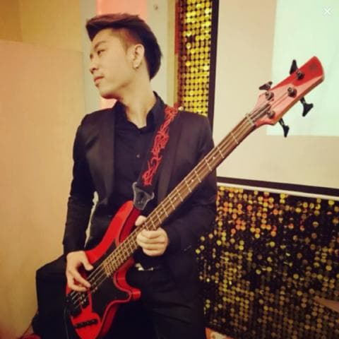 這張照片是一個年輕人拿著一把紅色電貝斯,他穿著黑色西裝外套,看起來很酷。