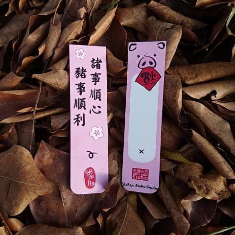 這張照片是兩張粉紅色書籤,上面寫著祝福語和圖案。左邊書籤寫著「豬事順心,諸事順利」,右邊書籤是一個可愛的小豬,上面寫著「福氣滿滿」和「Yuzhen Momo Studio」。