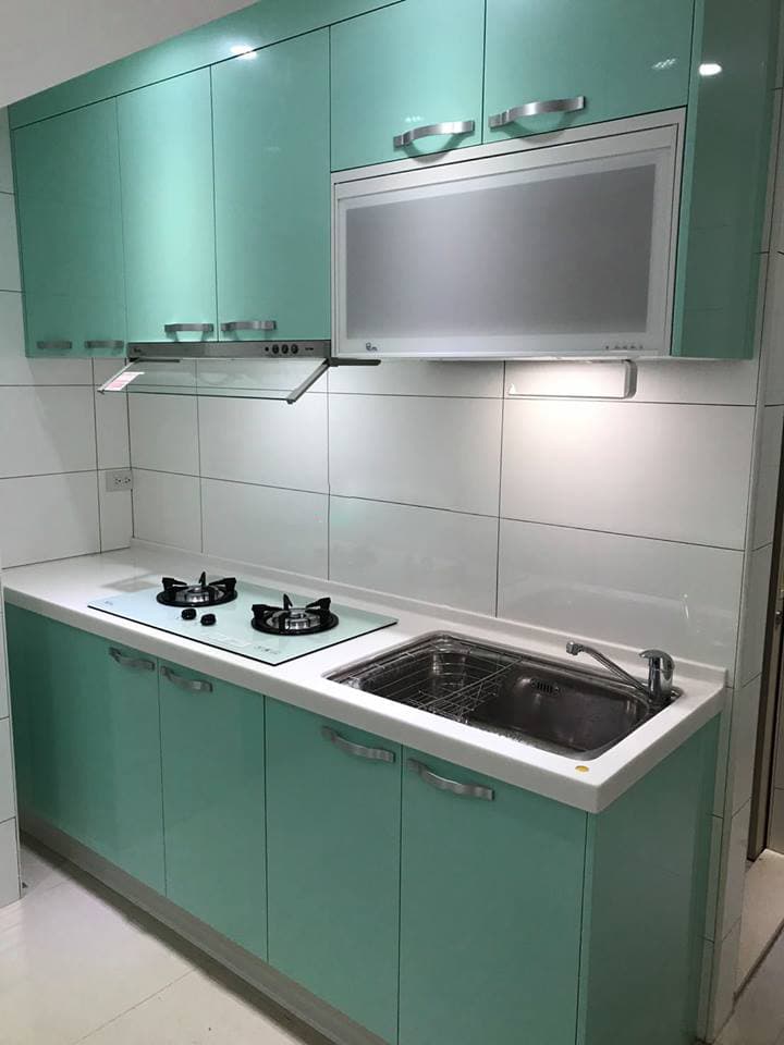 這張照片是廚房的一角,有水槽、流理台、瓦斯爐和櫥櫃。水槽和流理台的顏色為白色,櫥櫃為淺綠色,整體感覺乾淨清爽。