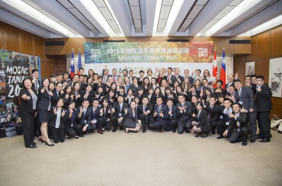 這張照片是一群人在會議室中參加一個活動,照片中的人們都很開心,他們都穿著正式的服裝,有些人在聊天,有些人則在拍照。最重要的是,他們都非常熱情地參與著活動。