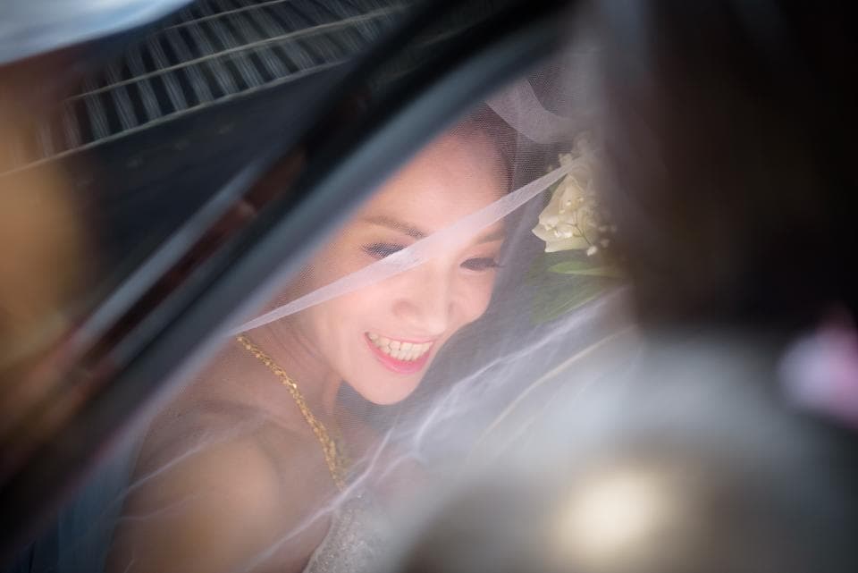 這張照片是一張新娘穿著婚紗,臉上蒙著頭紗,露出甜蜜微笑的照片。