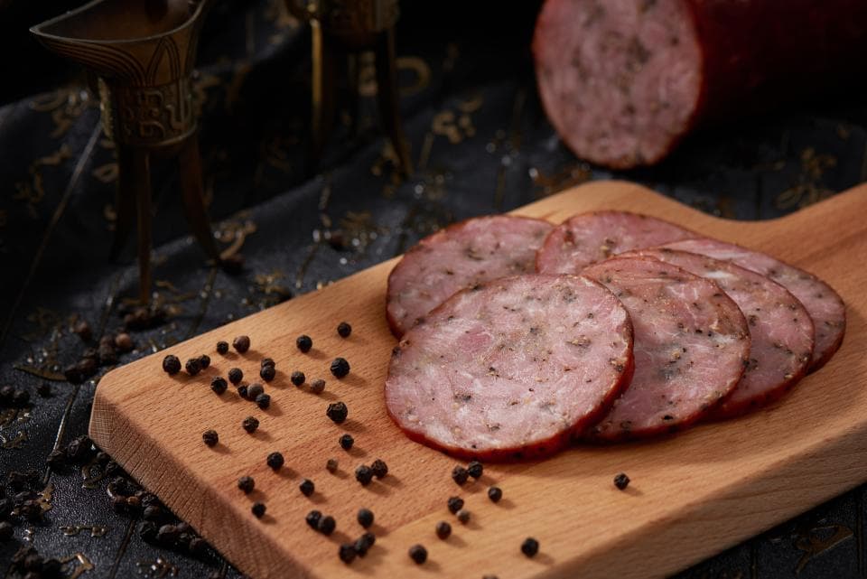 這張「香腸切片」的照片是一些切好的香腸放在木頭砧板上,旁邊有黑胡椒粒。